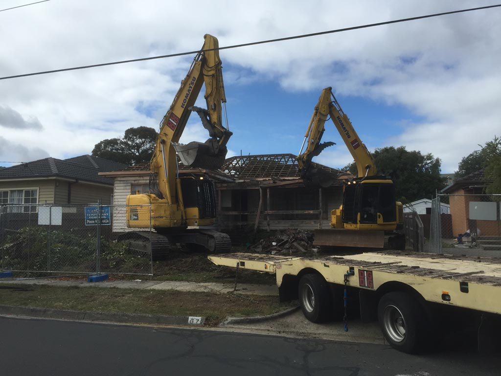 Two excavators demolishing a brick and weatherboard house on a residential street