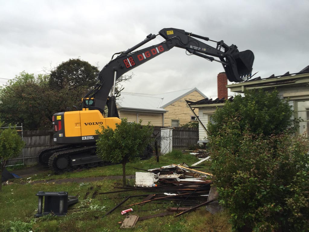 DigDig Demolition excavator beside a pile of timber and metal debris on a residential block