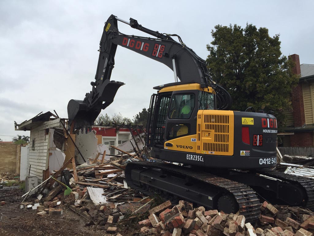 DigDig Demolition excavator demolishing a weatherboard house, with brick rubble in the foreground