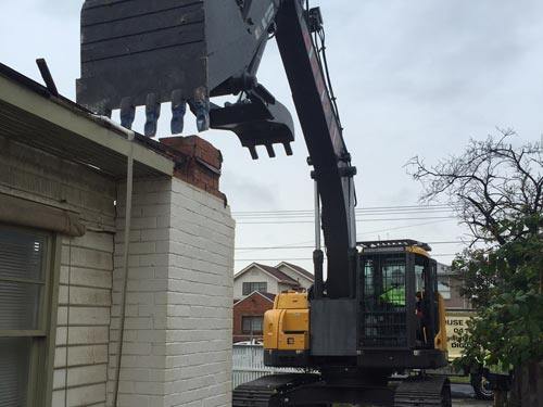 DigDig Demolition excavator removing roofing from the corner of a brick house