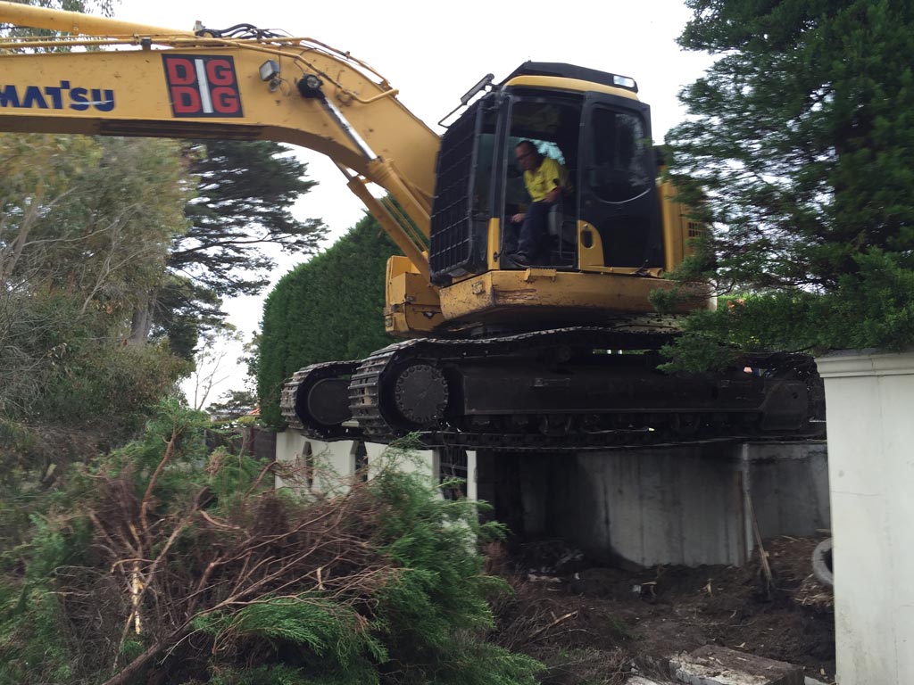 DigDig Demolition excavator working on top of a partially demolished house, arm extended with bucket