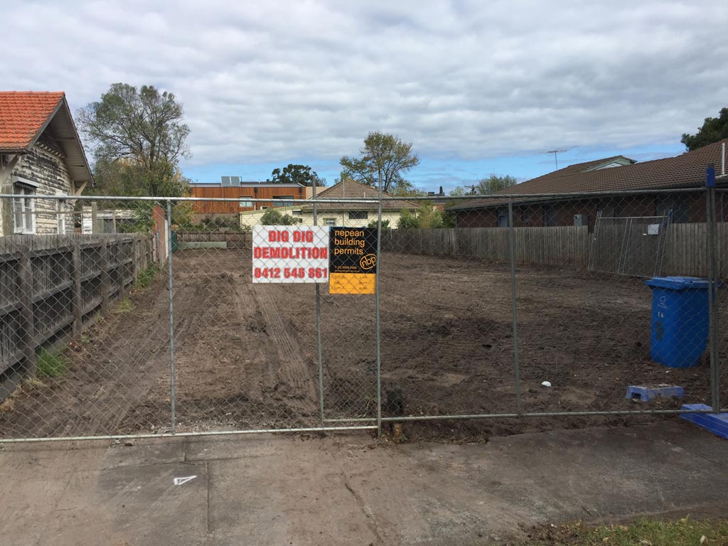 Cleared and levelled house block behind temporary fencing with a Dig Dig Demolition sign