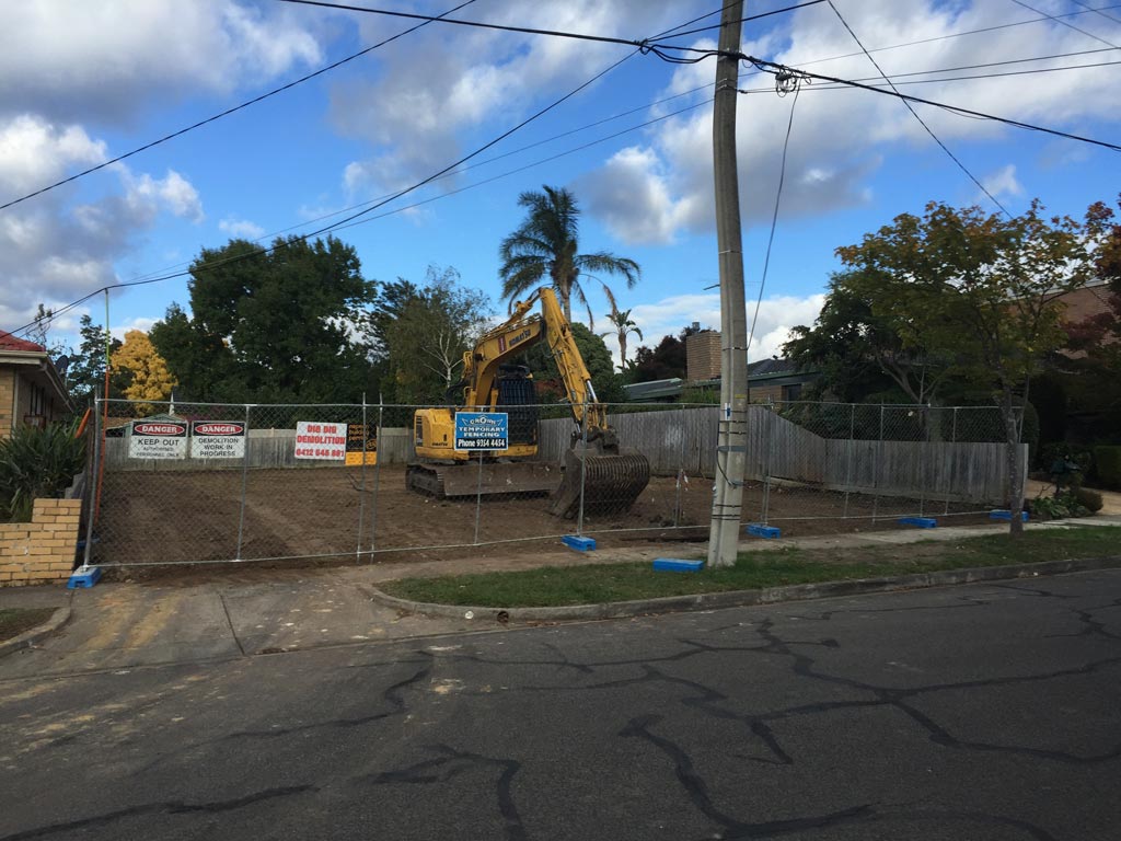 DigDig Demolition excavator on a fenced residential demolition site with danger and demolition-in-progress signage