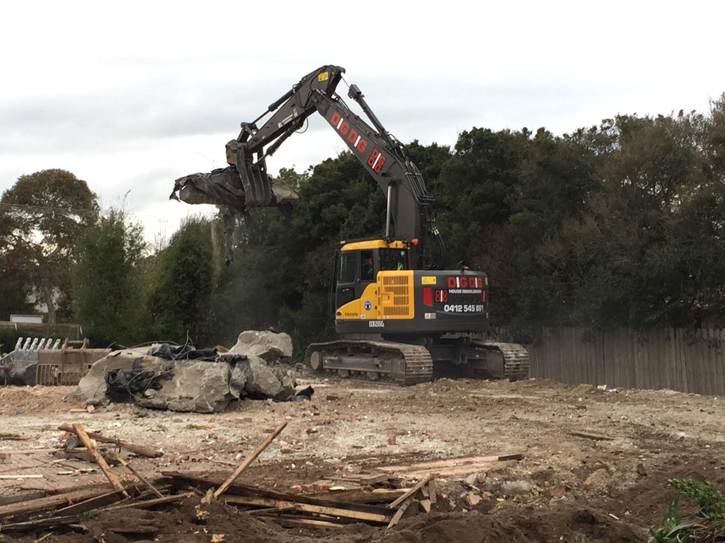 DigDig-branded excavator on a cleared demolition site with rubble piled beside a boundary wall